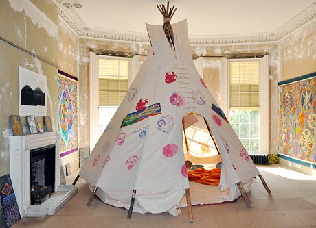 Photgraph of a teepee in the drawing room of a large Regency house, with colourful, patterned artworks on the walls